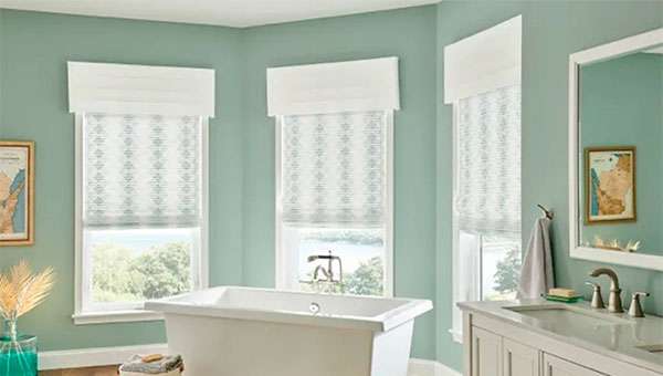 A large green bathroom with three windows with Graber cornices and fabric blinds.